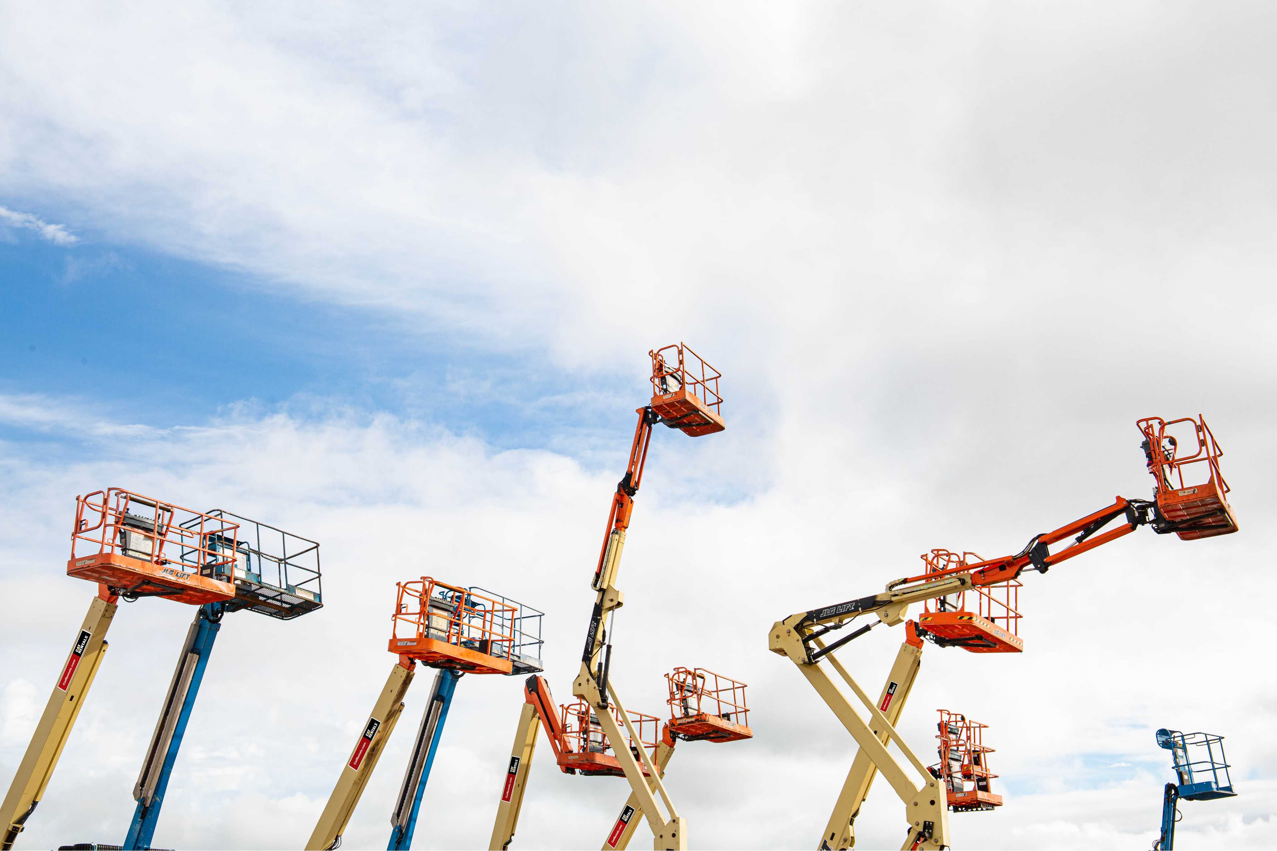 An array of Boom Lifts rising up to a cloudy blue sky.